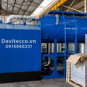 Lò hơi nằm ngang DAVITECCO màu xanh với thang tiếp cận, đường ống bọc cách nhiệt và cụm thiết bị phụ trợ trong xưởng