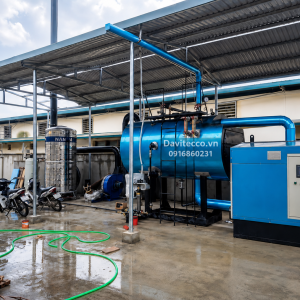 Hệ thống lò hơi nằm ngang DAVITECCO dưới mái che, gồm thân lò màu xanh, tủ điều khiển, bồn nước và đường ống
