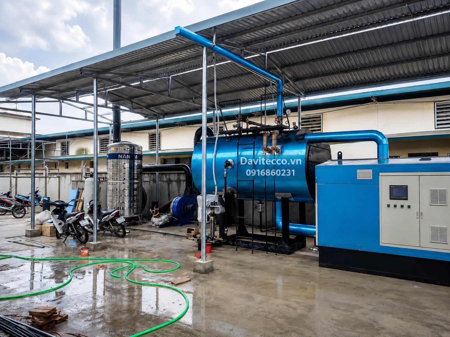 Hệ thống lò hơi nằm ngang DAVITECCO dưới mái che, gồm thân lò màu xanh, tủ điều khiển, bồn nước và đường ống