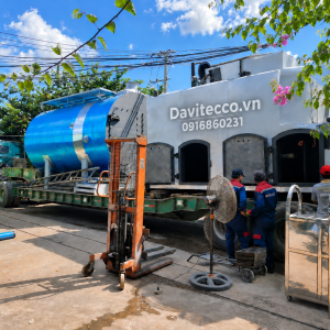 Thân lò hơi nằm ngang màu xanh và cụm buồng đốt DAVITECCO đặt trên xe vận chuyển, bên cạnh có nhân viên kỹ thuật